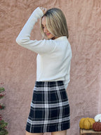 Woman wearing a black and white plaid mini skirt paired with a long-sleeve cream sweater against a neutral background.