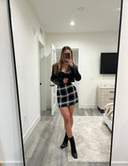 Woman wearing a black plaid mini skirt paired with a black blouse and ankle boots in a modern bedroom mirror selfie