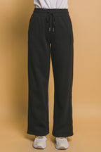 Black wide-leg sweatpants for women with drawstring waist and side pockets, styled with white sneakers.