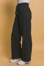 Woman wearing black wide-leg sweatpants with pockets and drawstring waist against beige background