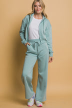 Woman wearing light blue wide-leg sweatpants with a matching zip-up hoodie and white t-shirt in casual style.