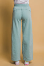 Back view of women's soft wide sweatpants in light blue paired with sneakers against beige background