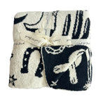Folded black and white plush blanket with abstract Western-inspired patterns tied with a cream ribbon