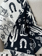 Cozy reversible black and white blanket with western-themed designs including cacti, horseshoes, stars, and boots.