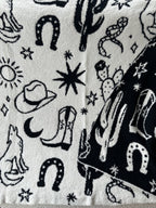 Cozy reversible blanket with black and white western-themed patterns including cowboy boots, hats, cacti, and stars.