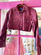 Cropped vintage-style western shirt in deep red with button front and flap pockets hanging on pink door frame