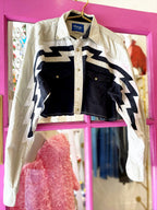 Cropped western style women's shirt with bold black and white zig-zag patterns and button front closure hanging on a pink frame.
