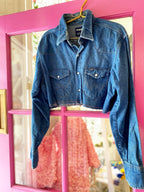 Cropped denim shacket with button-down front and two chest pockets hanging on a pink door frame