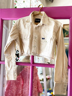 Cream cropped western shirt with collar and zig-zag hem hanging on a pink door frame in a women's clothing store.
