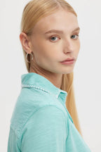 Woman wearing a sea-colored blouse with whipstitch detailing on the collar in soft breathable fabric