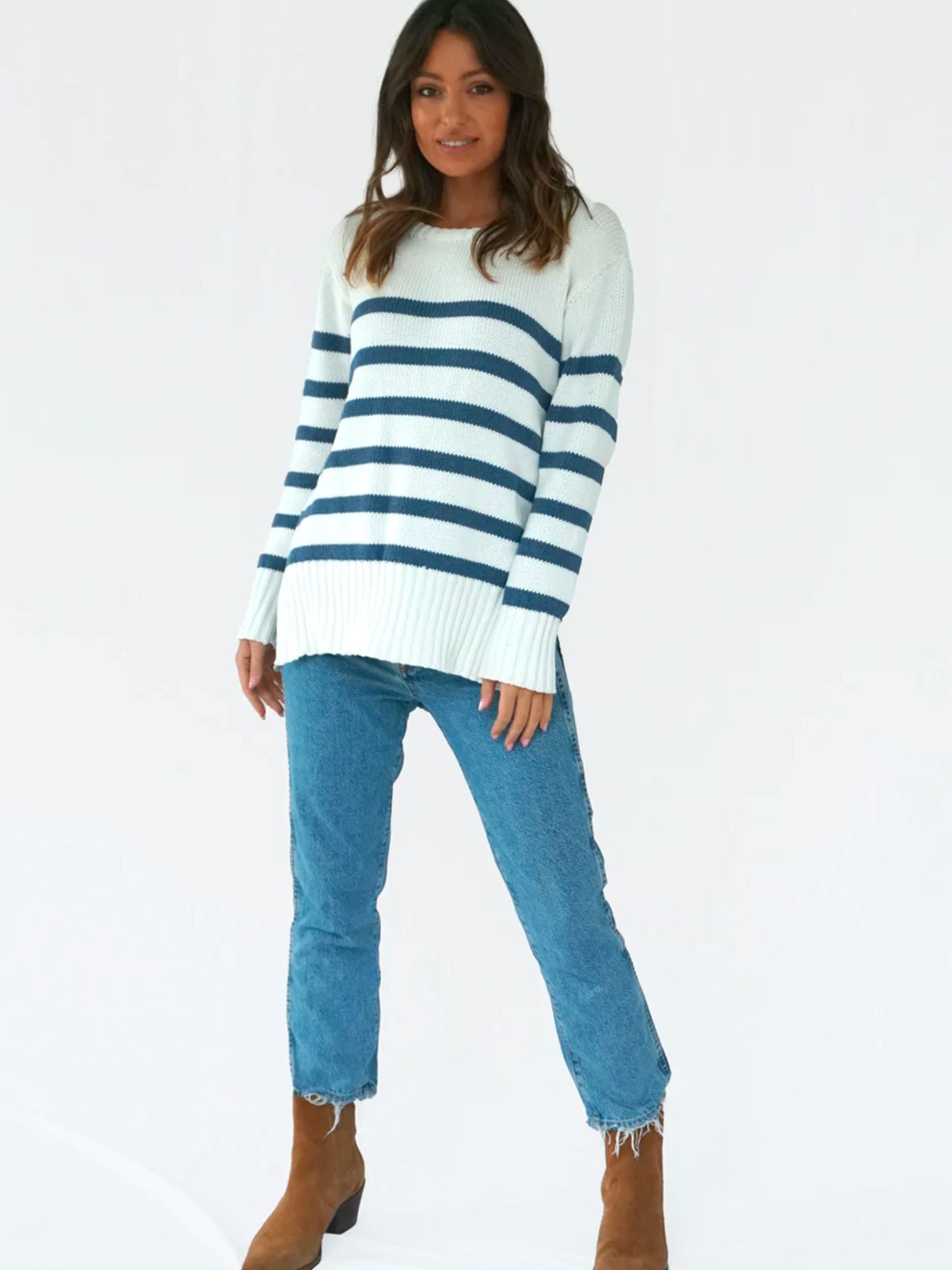 White sweater with blue horizontal stripes, spilt hem. Woman wearing weater with jeans and knee high brown boots