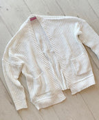 White oversized knit cardigan with pockets, open front, and textured pattern, laid flat on wooden floor.