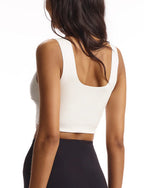 Woman wearing a white sleeveless crop top with a square neckline, paired with black high-waisted bottoms.