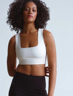 Woman wearing a white squareneck crop top paired with black high-waisted pants in a studio setting