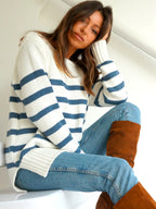Woman wearing a relaxed fit striped sweater with blue jeans and brown knee-high boots sitting indoors