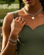 Woman wearing gold plated rings and layered chain necklaces with a green sleeveless top outdoors