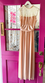 Sleeveless vintage-style women's dress with lace yoke and smocked waist in soft peach color hanging on door