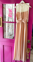 Sleeveless vintage-inspired women's dress with lace high neck and gathered waist hanging on a pink door.
