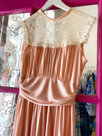 Women’s peach dress with lace high neck and smocked waist detail hanging on white hanger.