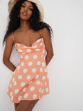 Woman wearing a peach polka dot mini dress with spaghetti straps and a cowl neckline, styled with a beige bucket hat