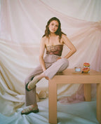 Woman wearing wide leg pants sitting on edge of table with grapefruit and drinks on it in soft pastel setting