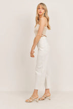 Woman wearing white wide leg pants and beige sleeveless top standing in profile against a plain background