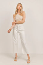 Woman wearing white wide leg pants with large pockets and a beige sleeveless top standing against a neutral background