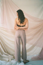 Woman wearing light-colored wide leg pants with roomy pockets, standing barefoot against soft draped fabric background