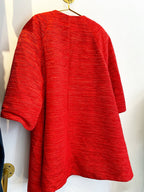 Red textured women's coat with a structured silhouette hanging on a gold hook against a white wall.