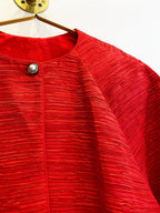 Red textured women's coat with rhinestone button closure on a gold hanger against white background