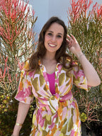 Woman wearing colorful sheer short sleeve top tied at waist outdoors among tall plants in women's clothing style