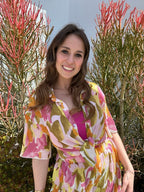 Woman wearing a colorful sheer short sleeve top tied at waist, standing outdoors near red and green plants