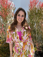 Young woman wearing a colorful patterned sheer top and matching bottoms outdoors among green and red plants