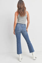 Woman wearing high-rise cropped flare denim jeans with raw hem and white boots against white background