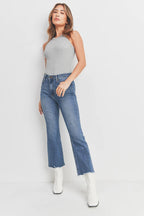Woman wearing high-rise blue cropped flare jeans with raw hem and white boots against a white background