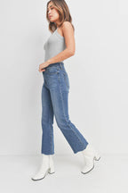 Woman wearing high-rise cropped flare denim jeans with raw hem paired with white heeled boots and gray tank top
